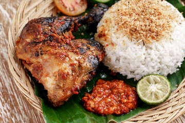 close up of grilled chicken with white rice and sambal served on a traditional woven plate