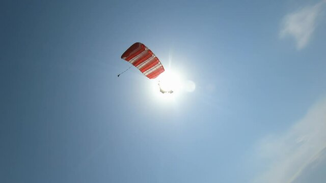 Extreme skydiver flying against a clear blue sky, sunbeam shines into camera