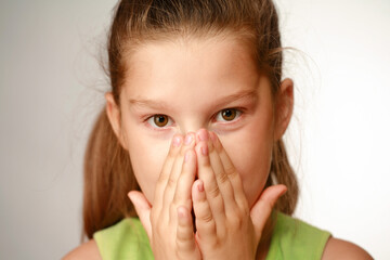 Little girl covering her mouth with hands on the light background.. Surprised or scared. shallow depth of field on the fingers.