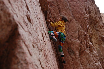 little boy climbs on the rock with rope