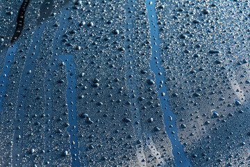 Naklejka na ściany i meble Water drops on a black surface. Dew on the hood of the car in the morning.