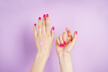 Beautiful hands of a young woman with a drop of cream on a purple background. Beautiful manicure flat lay.