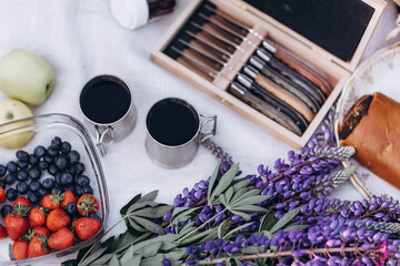 Family picnic with fruits and tea in a flowering field of lupins. Holidays and trips with family out of town on nature.