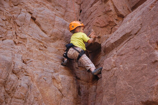 little boy climbs on the rock with rope