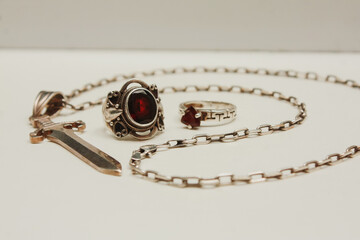 Silver pendant in the shape of a sword on an anchor chain, silver set of earrings and rings with natural red garnet stone, pendant in the shape of a lizard with transparent zircon on a white backgroun