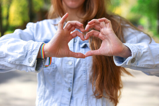 Faceless girl with LGBT bracelet makes heart with her hands. Heart shaped hands, pride concept