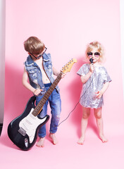 Pop Culture: Children a boy with a guitar and a girl with a microphone pretend to be popular musicians and perform a home concert.