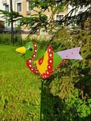 Garden figure - a multi-colored bird among trees and herbs
