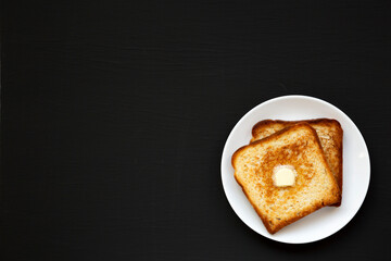 Homemade Buttered Toast on a white plate on a black background, top view. Flat lay, overhead, from above. Copy space.