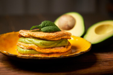 Low Carb Keto Diet Pancakes from almond coconut flour stack on plate with avocado mousse on wooden table background close up view. Selective focus. Ketogenic concept