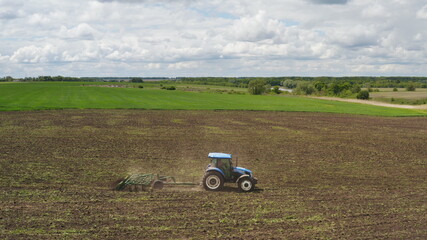 Fototapeta premium Aerial view of a farmer on a tractor with a cultivator working in the field, crust removing, soil aeration and lifting young weeds. Ground preparation before re-sowing crops