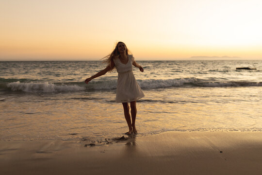 Caucasian woman standing barefoot on a beach during sunset