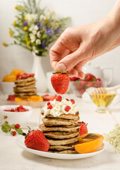 Pancakes with strawberries, delicious breakfast. A woman decorates strawberries with a stack of pancakes with whipped cream. vertical food photo