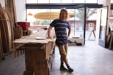 Caucasian male surfboard maker in his studio working with surfboards in the background