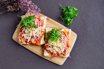 Baked hot sandwiches on white bread with fried vegetables in tomato sauce, Servelat straws, melted cheese and green watercress on a wooden Board