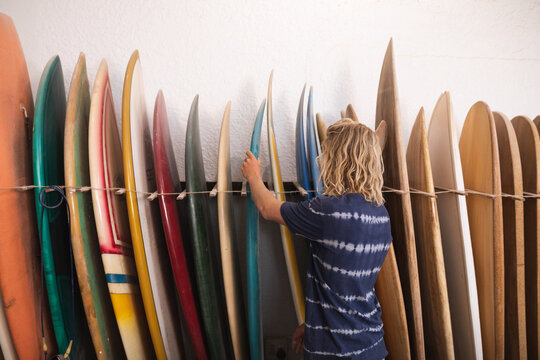 Caucasian male surfboard maker in his studio checking one of the surfboards standing with surfboards