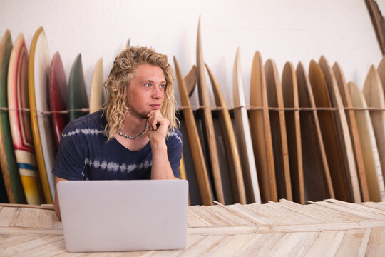 Caucasian male surfboard maker in his studio working with surfboards in the background