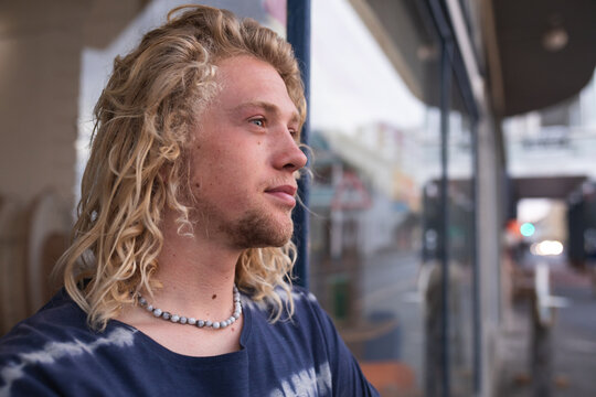 Caucasian male surfboard maker leaning on a door of the entrance with surfboards in the background