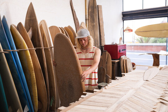 Caucasian male surfboard maker in his studio inspecting one of the surfboards