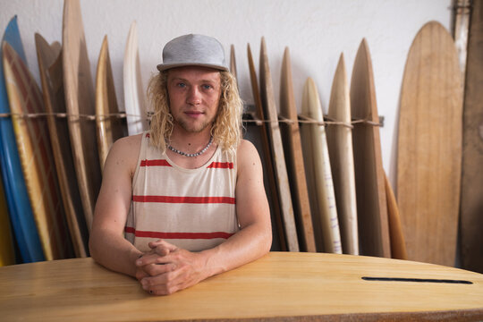 Caucasian male surfboard maker in his studio, holding one of the surfboards and smiling to camera