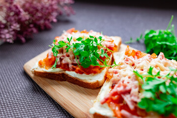 Baked hot sandwiches on white bread with fried vegetables in tomato sauce, Servelat straws, melted cheese and green watercress on a wooden Board