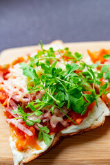 Baked hot sandwiches on white bread with fried vegetables in tomato sauce, Servelat straws, melted cheese and green watercress on a wooden Board