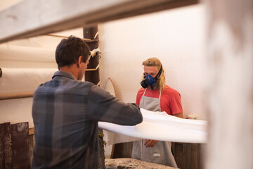 Two Caucasian male surfboard makers making a wooden surfboard together and polishing