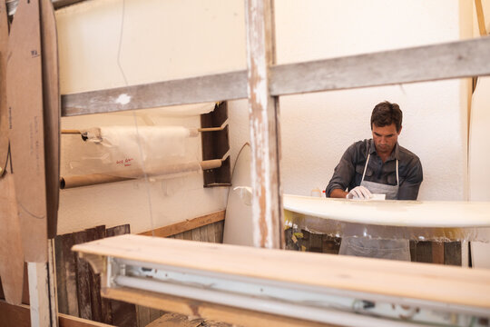 Caucasian male surfboard maker preparing a wooden surfboard covered with a white piece of cloth