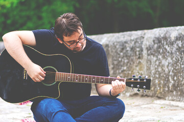 Obraz premium Young man playing guitar sitting on the bridge
