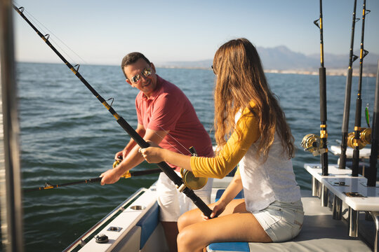 A Caucasian man and his teenage daughter holding fishing rods and talking