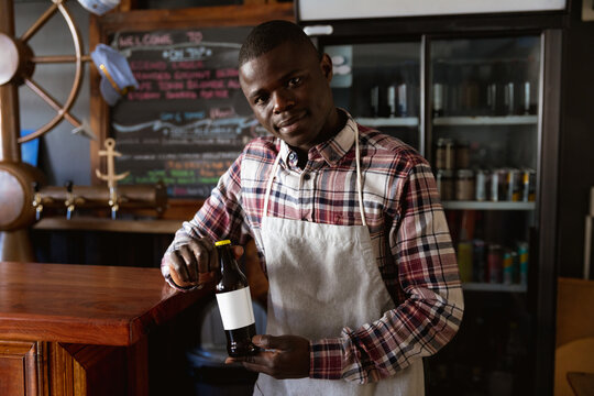 Portrait of an African American barman in a brewery holding a beer bottle