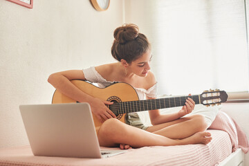 Chica aprendiendo a tocar la guitarra con ordenador delante
