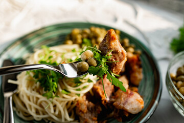 A hearty meal on the table, spaghetti with fried pork chunks, green canned peas and watercress grass. Next to the sauce and a bowl of peas. Green interesting plate