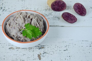 Vitelotte mashed purple potato in a bowl garnish with parsley.