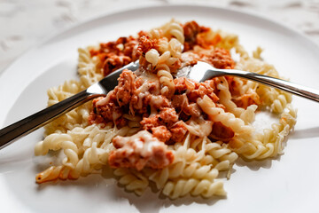 A simple dish on a white plate with boiled pasta in the form of spirals and meat Bolognese sauce in tomato paste, a hot dish with melted cheese.