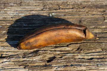 A spotty brown mini banana on an old textured wooden board under the sun. This fruit is suitable for baking banana bread