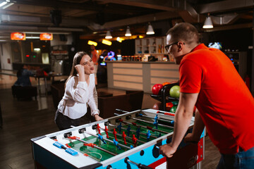 A beautiful young caucasian girl mocks and climbs a man while they play table football. Love and fun