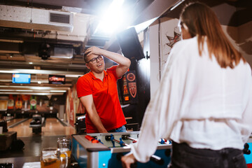 Obraz premium A beautiful caucasian girl and a man with glasses play table football in the playroom. Love and fun time