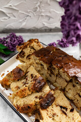 A large pie, cut into portions, stuffed with fruit and berries, among the branches of purple lilac blooming in spring. Homemade cakes on a tea tray.