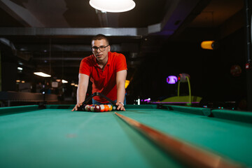 A young caucasian man in a red T-shirt places balls on a pool table. Fun time 