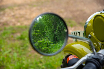 The forest is reflected in a motorcycle mirror.