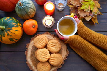 Top view cup of tea with mint in female hand. Homemade peanut cookies, pumpkin and autumn yellow leaves on wooden background.