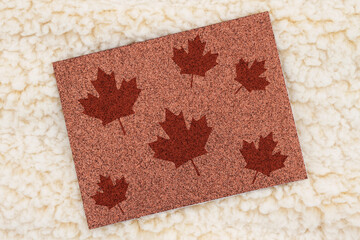 Blank brown glitter greeting card with maple leaves on beige plush fabric mockup