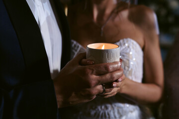 Loving bride and groom holds burning candle close-up at a wedding celebration