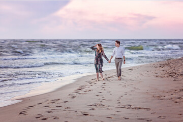 A young couple in love walk along the sea on the sand barefoot holding hands. They look at the sea. Love, trust, always be together concept
