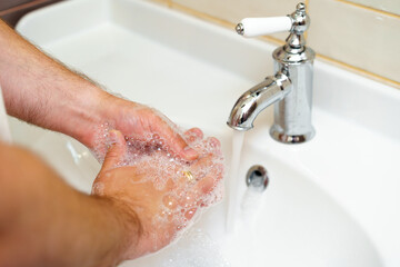 Close up photo of male hands washing with soap above the sink