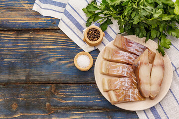 Raw fillet of saithe. Fresh slices on a plate, spices, parsley. A bunch of greens, vintage napkin