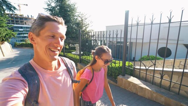 Young couple taking selfie portrait during walking sunny empty road with green fence. Man and woman takes selfie while traveling having fun discovering and sightseeing