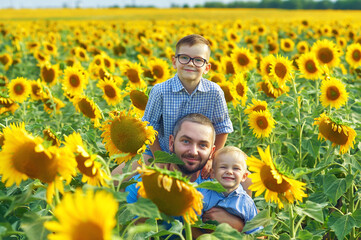 A young father with two sons on a walk in a field with sunflowers