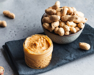 Closeup peanut butter in a glass jar, a handful of peanuts in shell. Foodphoto. Copy space. Breakfast for vegetarians.